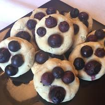 An image of Blueprints Blueberry Dog Treats on a plate. The treats are made with milk, eggs, honey, gluten-free flour, salt, and blueberries. The blueberries are arranged in a paw pattern on top of the cookies.