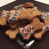 An image of homemade dog bone shaped peanut butter dog treats. Optional corn starch icing and sprinkles are shown on one side of the treats.