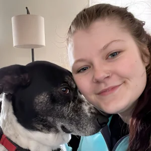 Audrey, a Four Seasons For Paws Home and Pet Guardian with a black and white dog nuzzling her cheek.