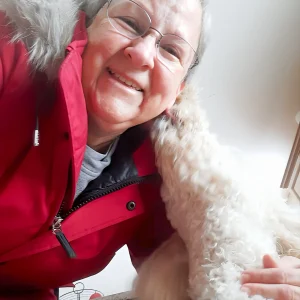 Colleen, a Home and Pet Guardian in Brighton with a white golden doodle kissing her cheek.
